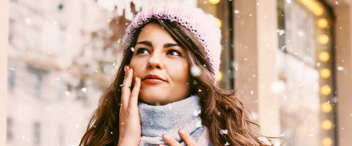 A woman touching her cheek while standing in a flurry of snow.