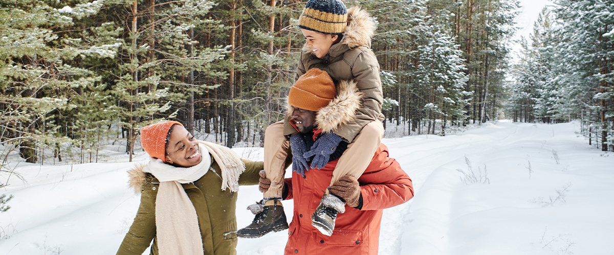 A family walks through the snow: a woman, a man and a small child sitting on the man's shoulders.
