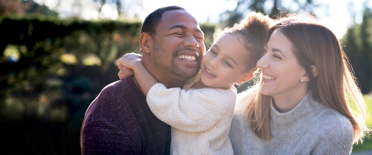 A couple and a young child smiling and hugging outside.