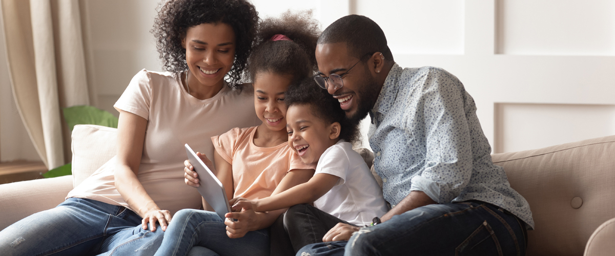 Family sitting on a couch looking at an iPad.