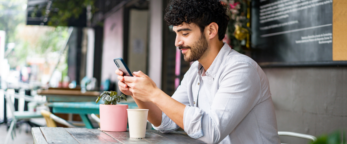 A young man using his phone while sitting outdoors at a cafe.