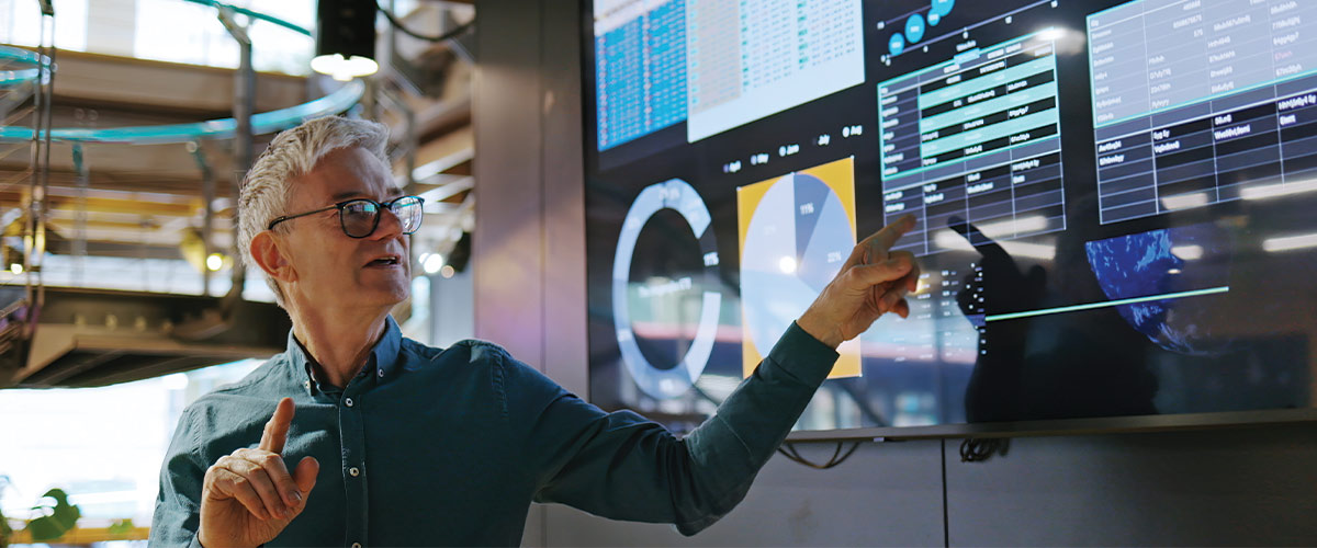 Person pointing at a digital screen containing various charts and graphs.