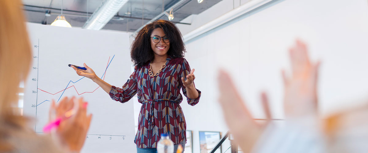 Woman presenting information to a group form a white board..