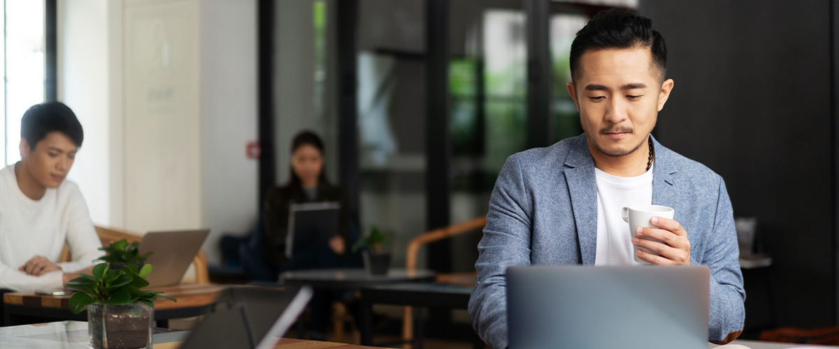 Man working on a laptop holding a mug.