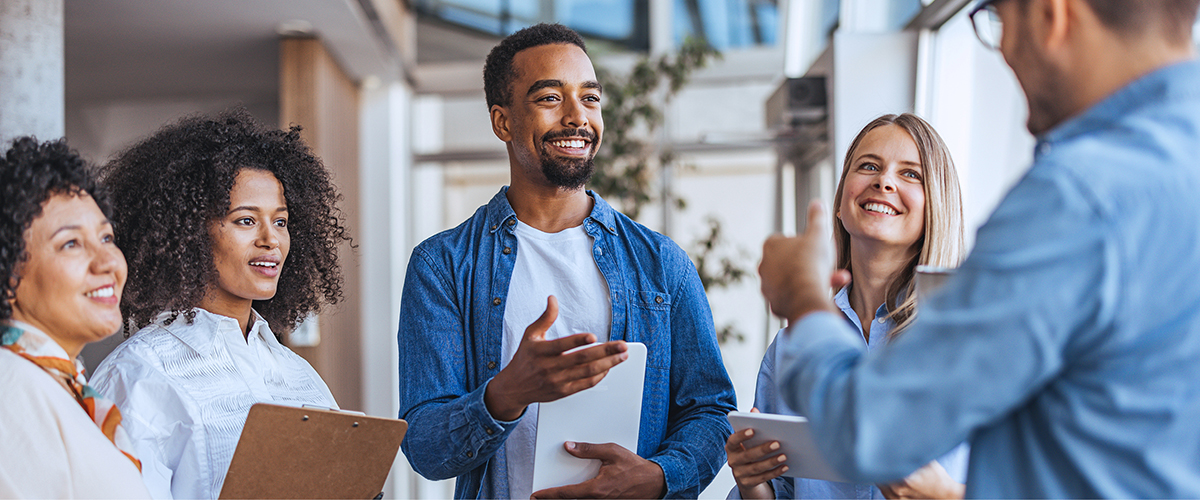Group of 5 colleagues chatting together in an office setting.