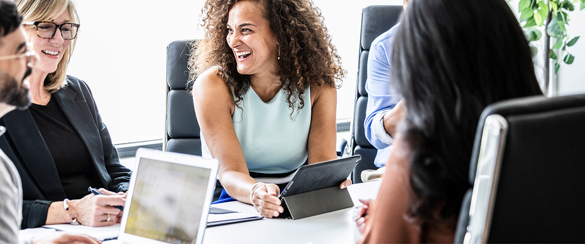 Group of coworkers in an office setting laughing together at a table.
