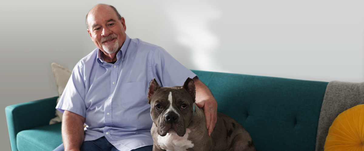 Senior man sitting on a couch with a dog.