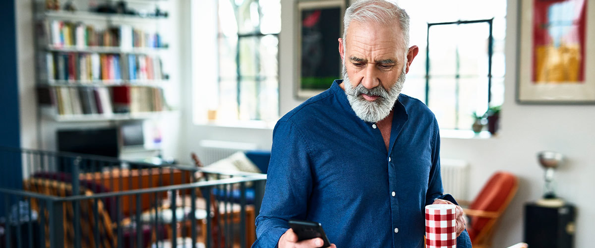 Senior man holding a mug and looking at a phone.