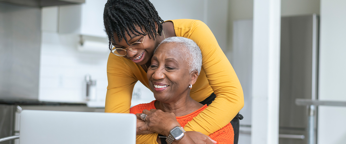 Granddaughter hugging her grandmother while looking at a laptop.