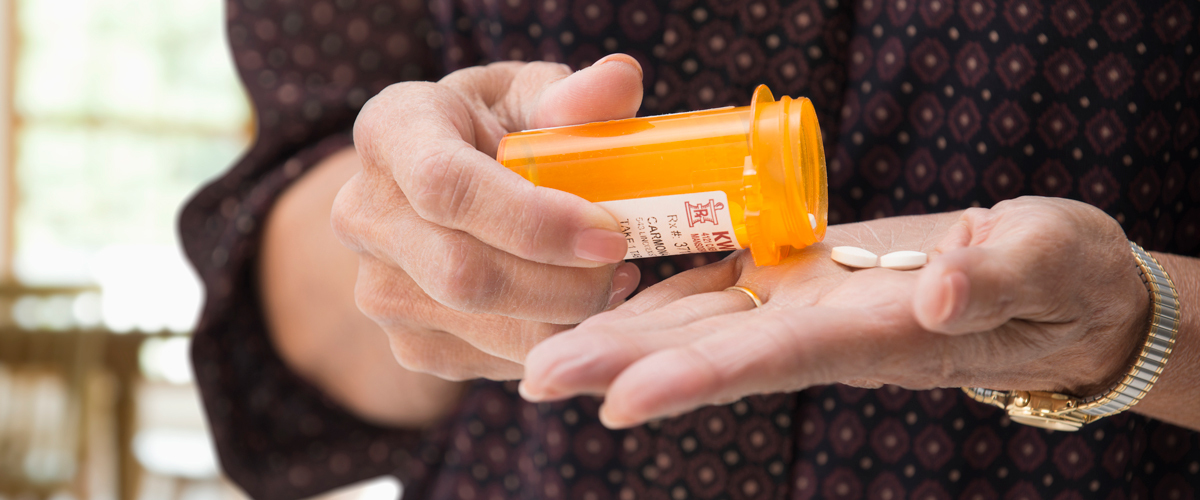 Hand taking medication out of a prescription pill container.