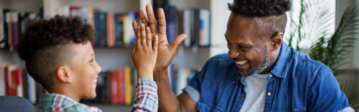 Adult and child smiling, high-fiving in front of a bookcase.