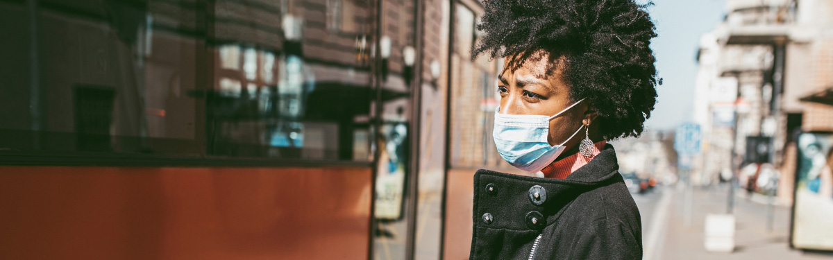Woman wearing a mask, standing outside at a train station.