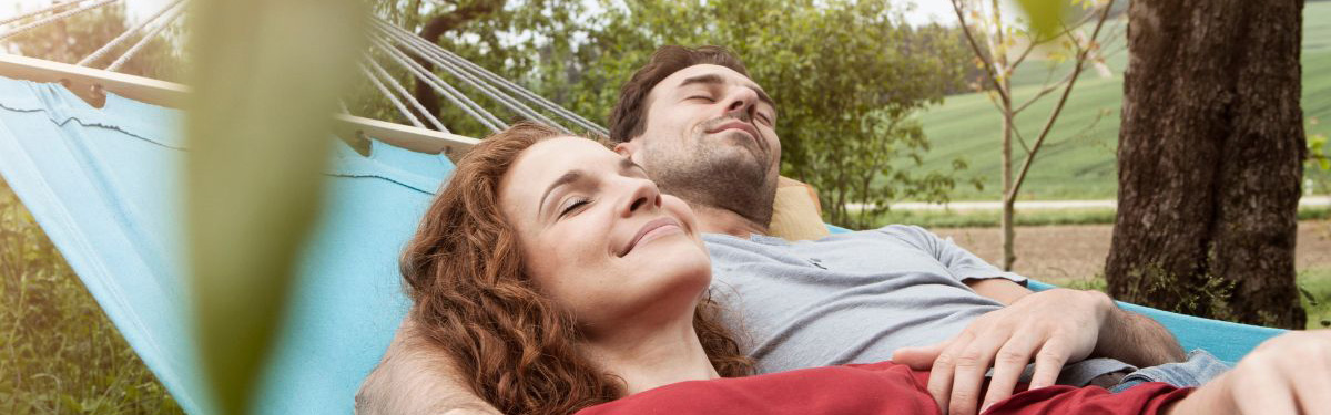 A man and woman resting outdoors on a hammock.