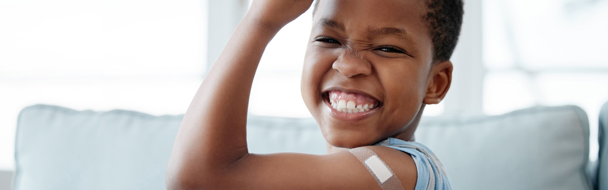 Child flexing his arm showing off a bandage from an immunization.
