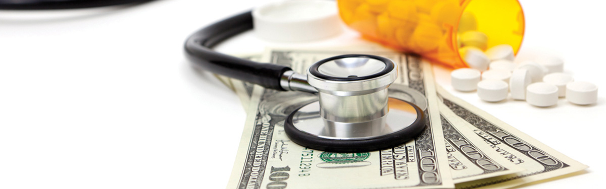 A bottle of prescription pills, a stethoscope and three 100 dollar bills laid out on a table.