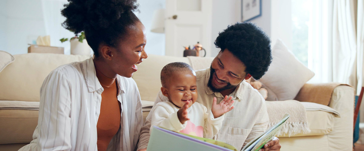 Caregivers and a young child reading a book together in a living room.
