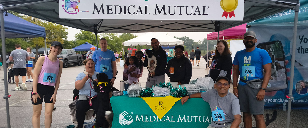 Group of runners gathered around a Medical Mutual table at an outdoor race event.