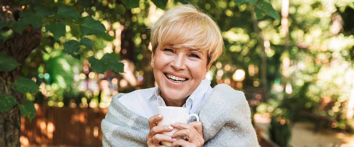 Person holding a white mug while sitting outdoors in a sunlit garden.