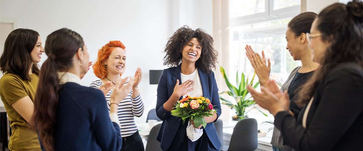 A group of employees celebrating a coworker with a bouqet of flowers and clapping.